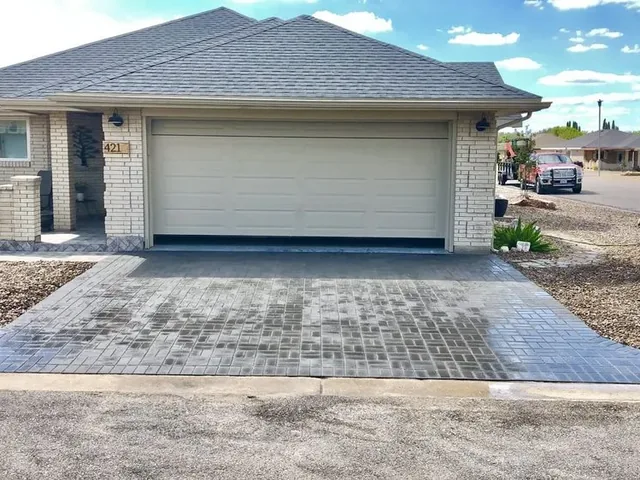 A gray paver driveway running the full width of a frontage to a two-car garage, with a low brick planter wall to one side