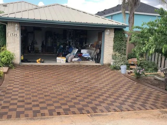 A driveway laid over its whole area in a checkerboard of dark brown and tan pavers, running up to an open garage