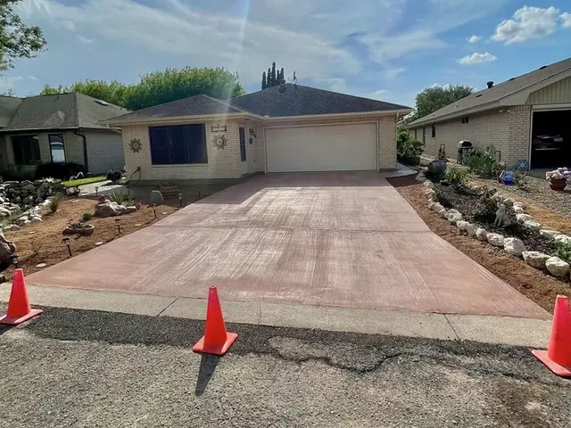 A poured concrete driveway with the ground either side not yet made good and traffic cones set out at the curb