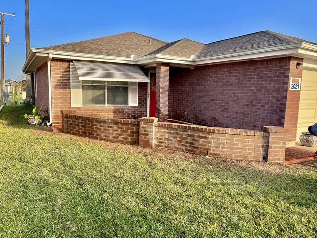 The corner of a red brick house with a low brick planter wall along the front and a natural grass lawn