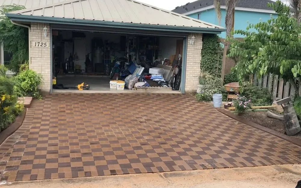 The same driveway after the work: laid over its whole area in a checkerboard of dark brown and tan pavers, edged and run up to the garage opening