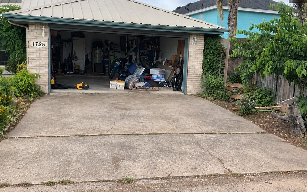 The same driveway before the work: plain gray concrete in slabs, cracked across the middle and weeded along the joints, running up to the open garage