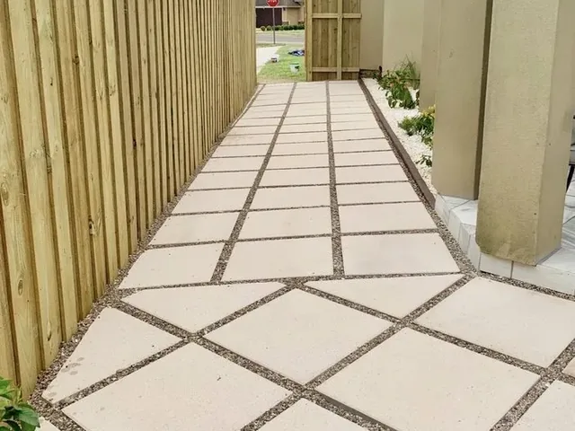 A side-yard walkway running between a tall wooden fence and a stucco house wall out to a wooden gate