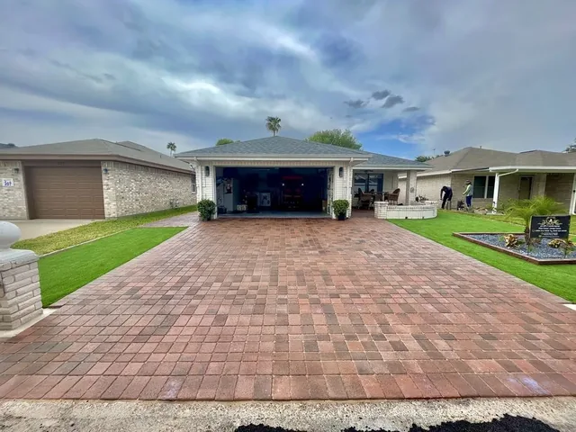 A wide red and tan paver driveway running up to an open garage, with strips of lawn let in down both sides