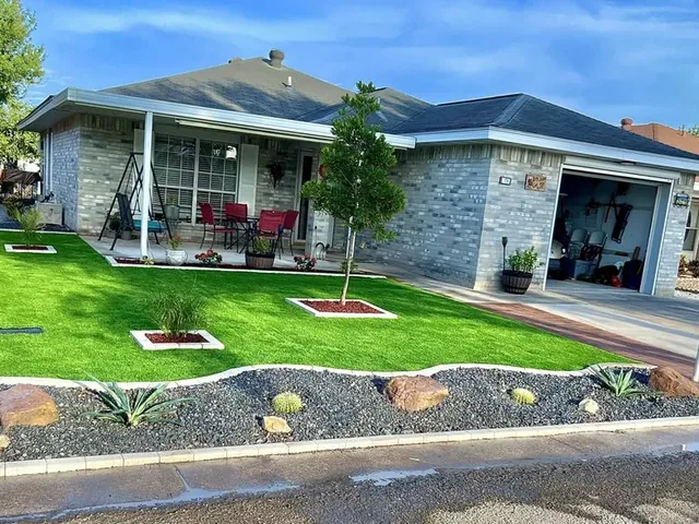 A front lawn with mulched square cut-outs let into it, edged by a cream curb laid to a wave and a dark gray gravel bed planted with cacti